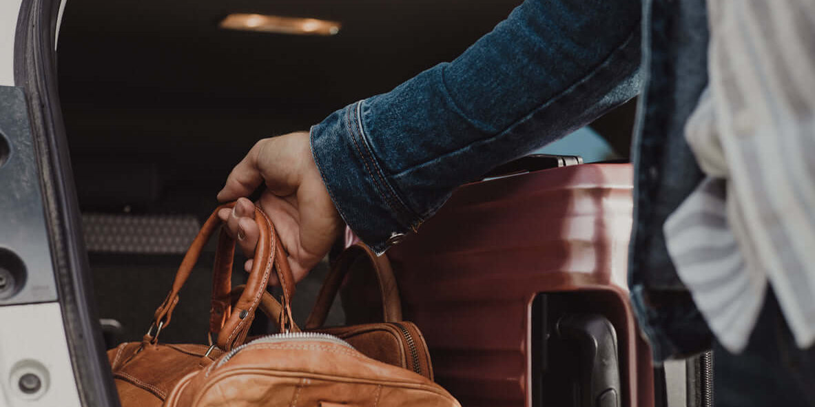 Homme prenant un élégant sac en cuir brun dans le coffre d'une voiture, évoquant le style masculin avec élégants sacs pour homme.