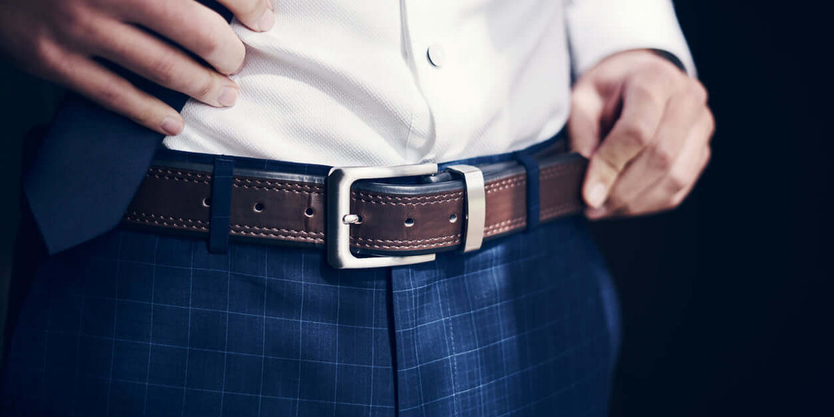 Homme ajustant sa ceinture sur un pantalon homme élégant avec chemise blanche et veste.