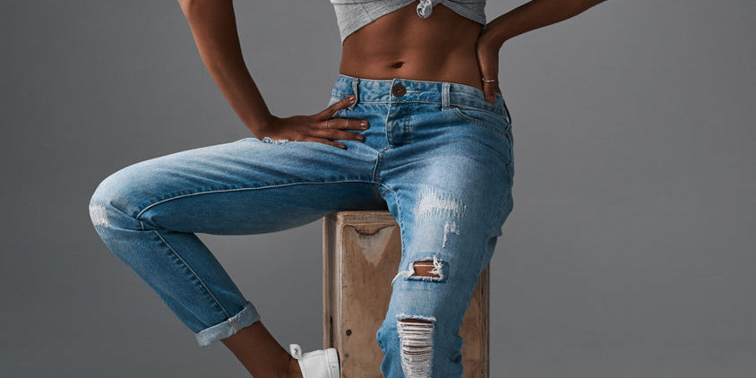 Femme sportswear tendance avec un top gris et un jean déchiré, présentant un style décontracté.