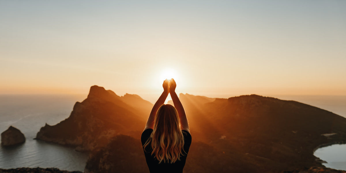 Femme méditant au coucher de soleil avec les mains levées, illustrant le calme et l'harmonie, parfait pour le yoga apparel and accessories.