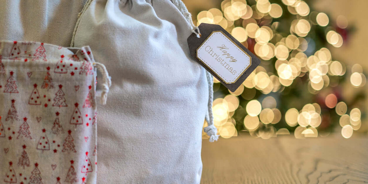 Sacs à langer et trousses bébé élégants avec un tag 'Happy Christmas' sur fond de sapin de Noël décoré.