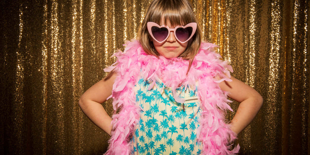 Fille portant des vêtements pour fille élégants avec des lunettes de soleil et un boa en plumes roses.