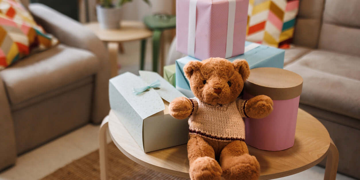 Un ours en peluche sur une table, entouré de boîtes cadeaux, représentant des jouets faits main pour enfants.