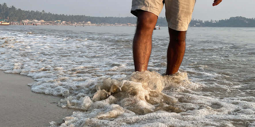 Man walking in elegant mens shorts bermudas along the beach waves, enjoying a sunny summer day.