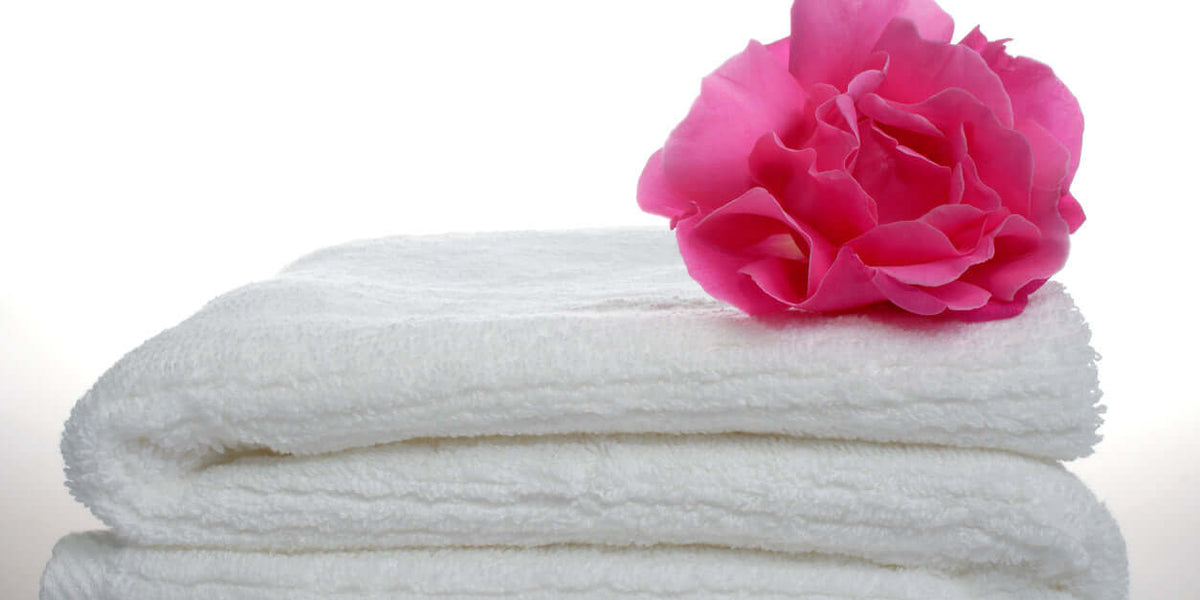 Lessive douce multi-taches, serviettes blanches empilées avec une fleur rose sur le dessus.