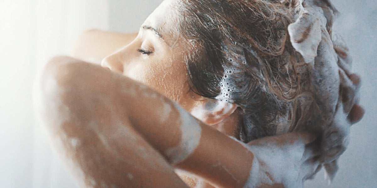 Femme se lavant les cheveux avec des savons et soins lavants intimes, profitant d'un moment de bien-être sous la douche.