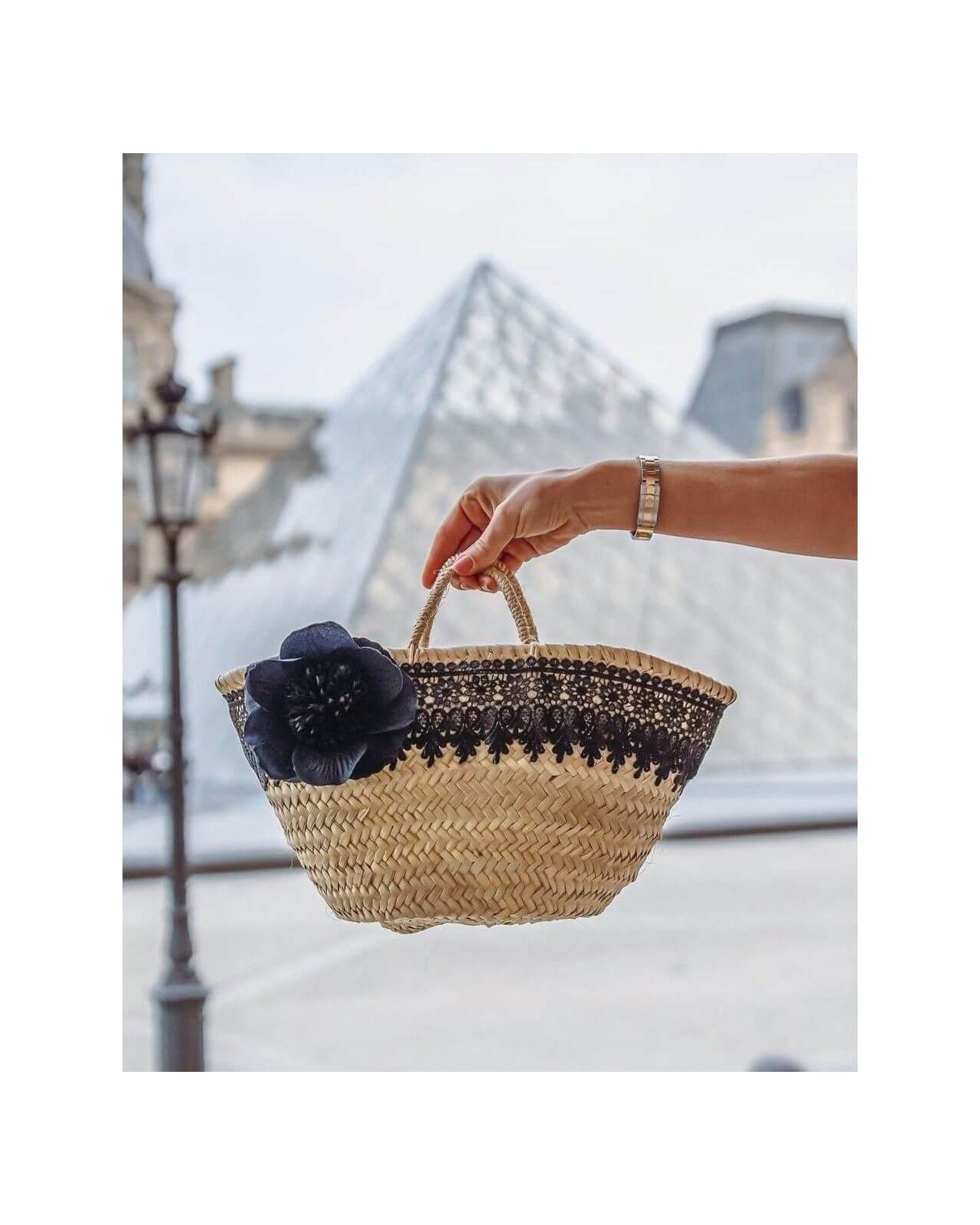 Petit panier noir élégant avec une rose noire, au pied de la pyramide du Louvre.