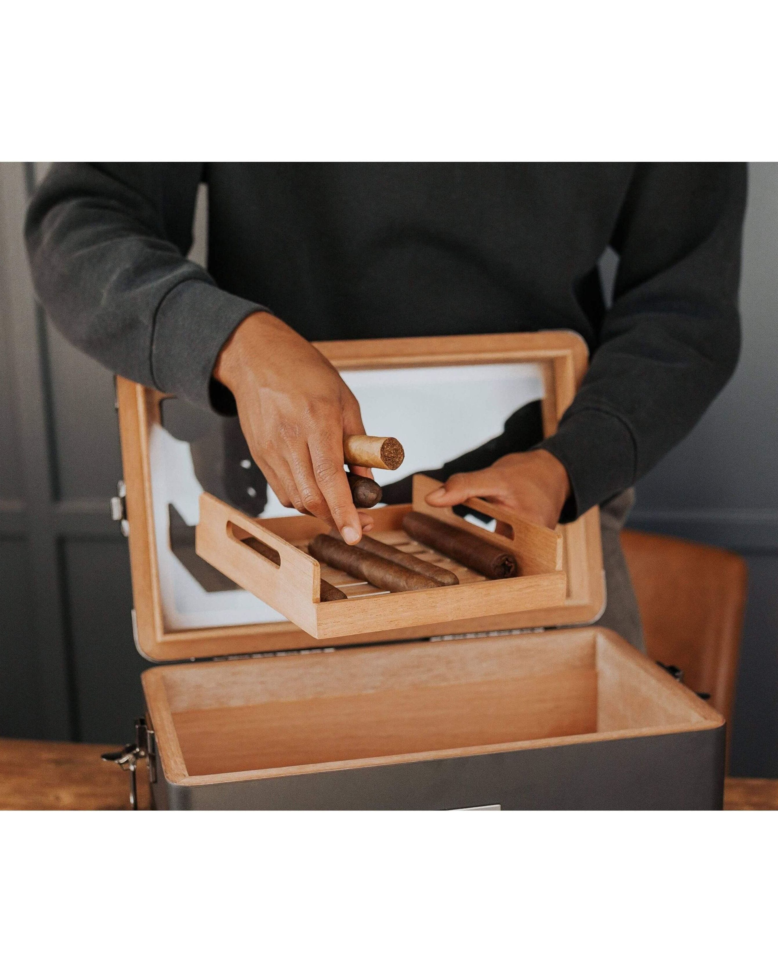 Person holding cigars in a unique black humidor, showcasing the craftsmanship and cedar wood inlay.