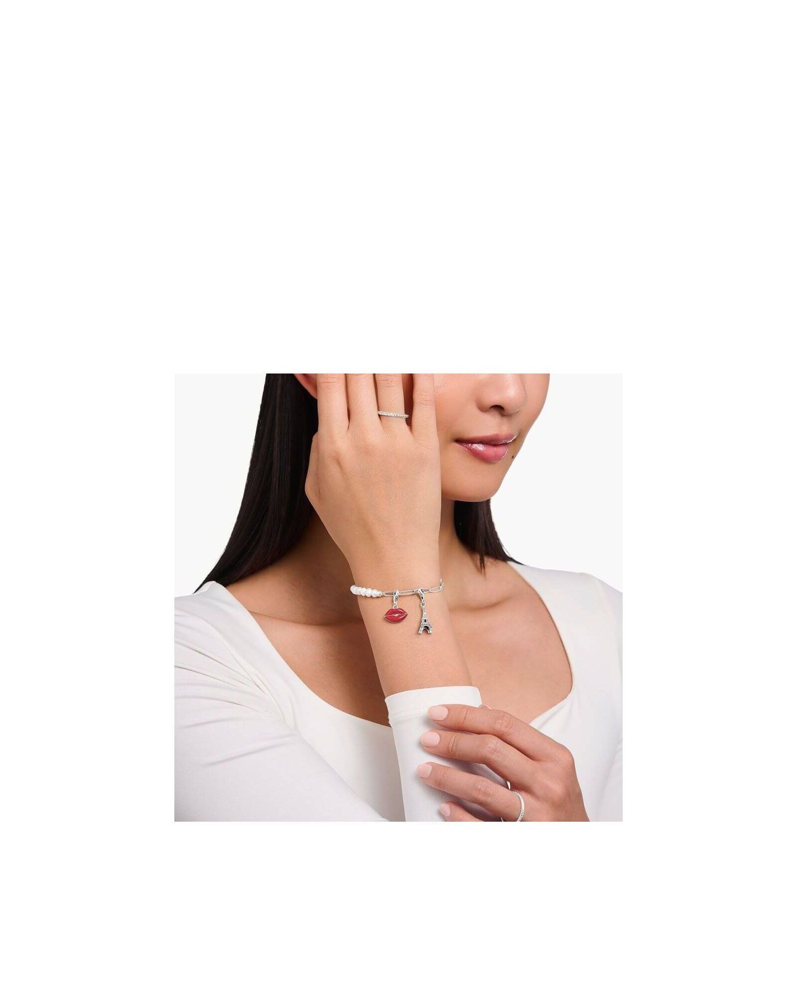 Bracelet charm featuring Eiffel Tower and red lips charm, worn elegantly by a woman.