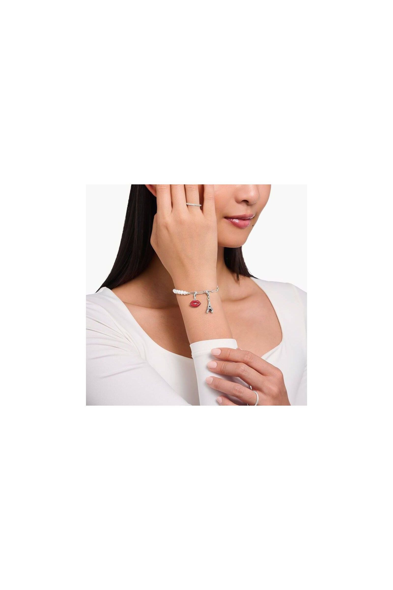 Bracelet charm featuring Eiffel Tower and red lips charm, worn elegantly by a woman.