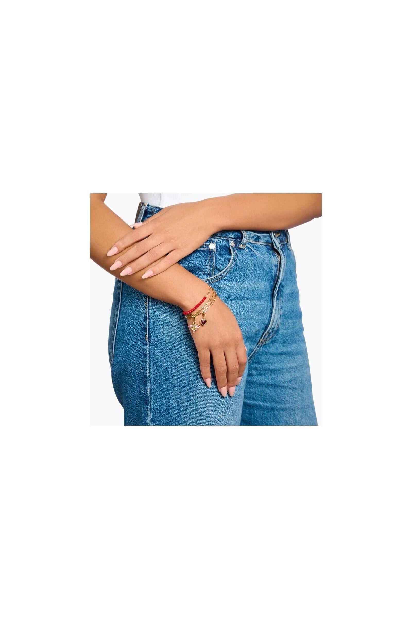 Femme portant un bracelet ajusté avec des perles rouges et un coeur, sur un fond en jeans.
