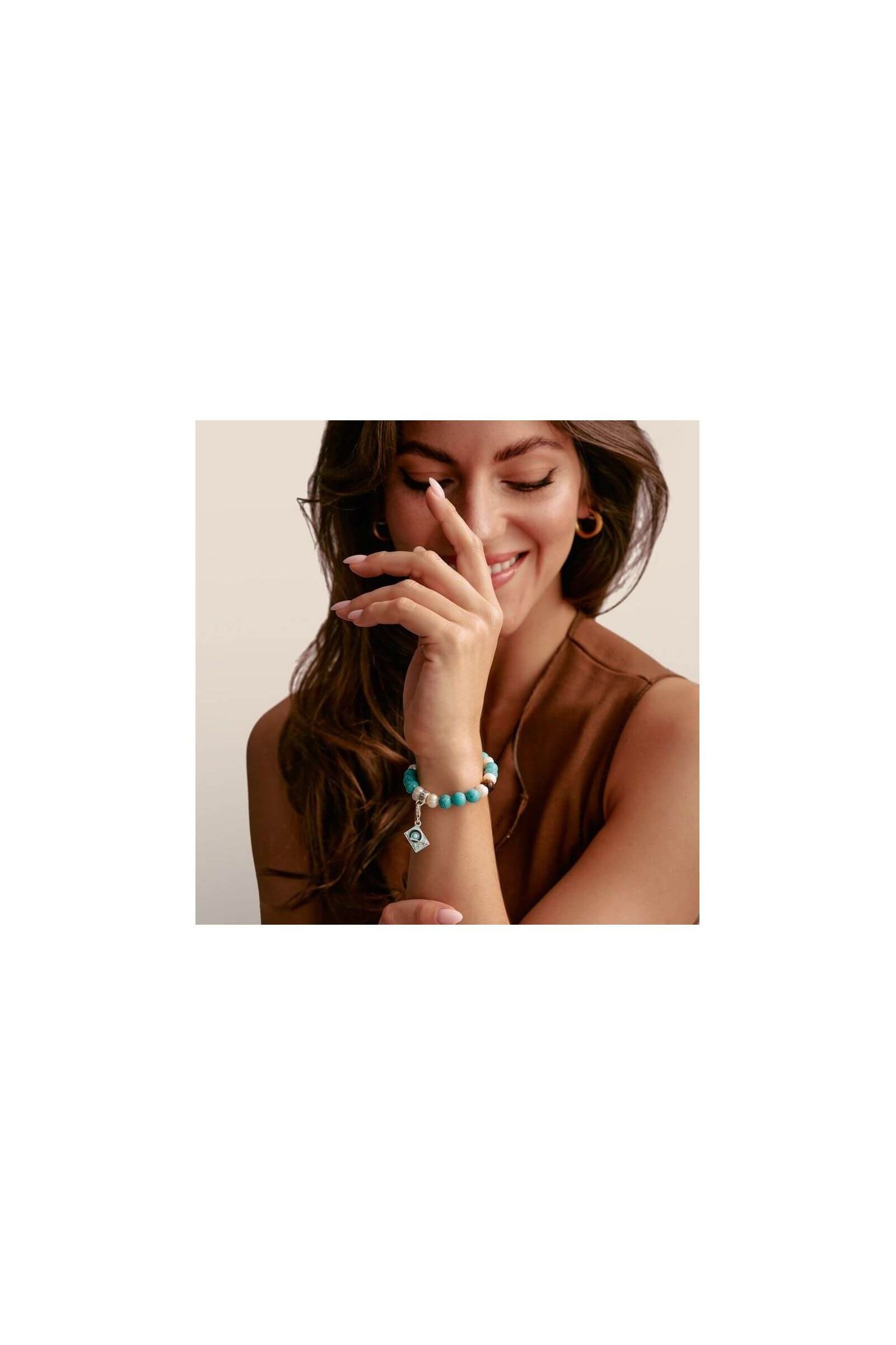 Femme souriante portant un bracelet coloré en perles turquoise, accentué par un charm élégant.