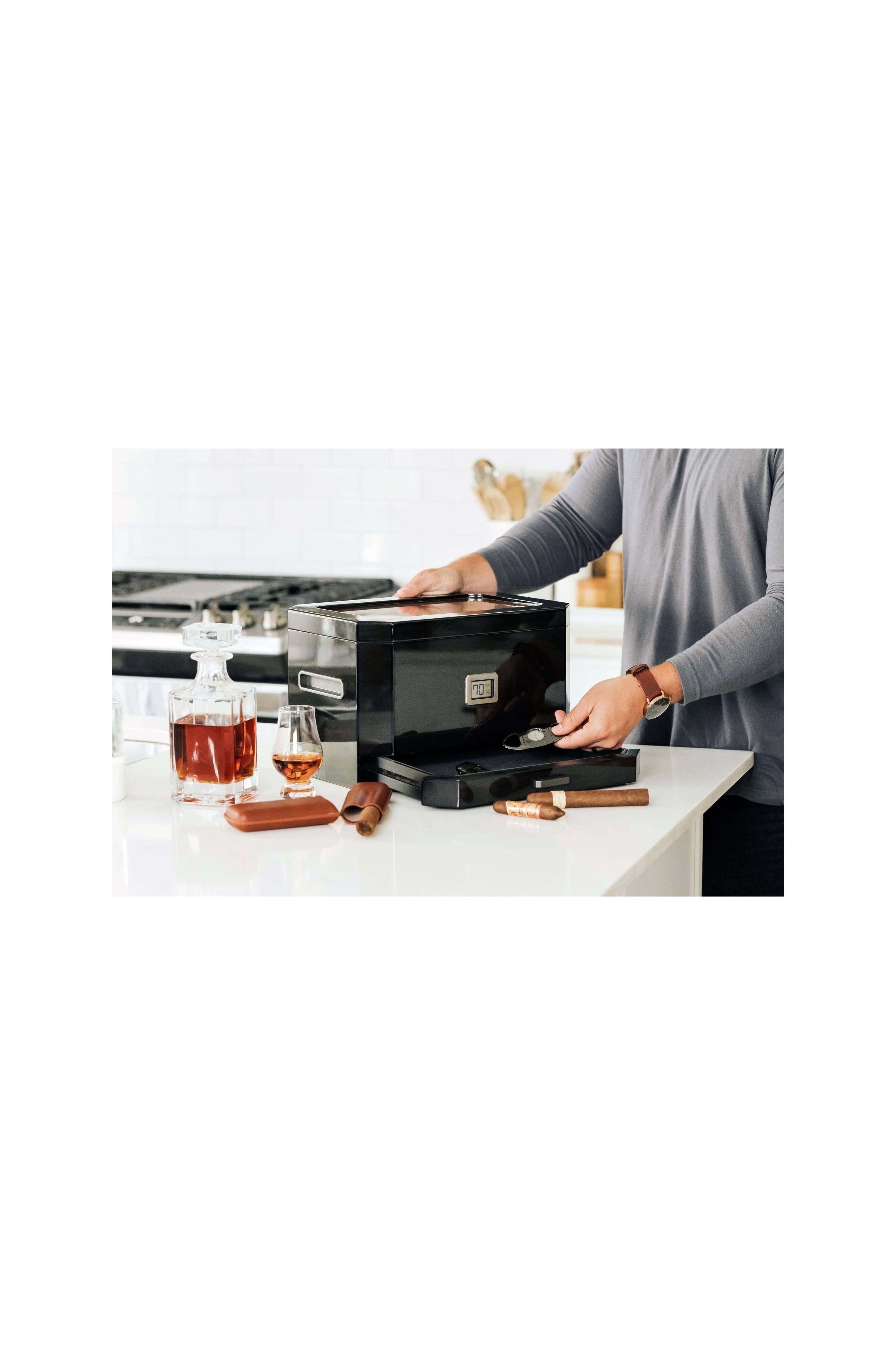 Homme utilisant un humidor à couvercle en verre Octodor dans une cuisine moderne avec des cigares et du whisky.
