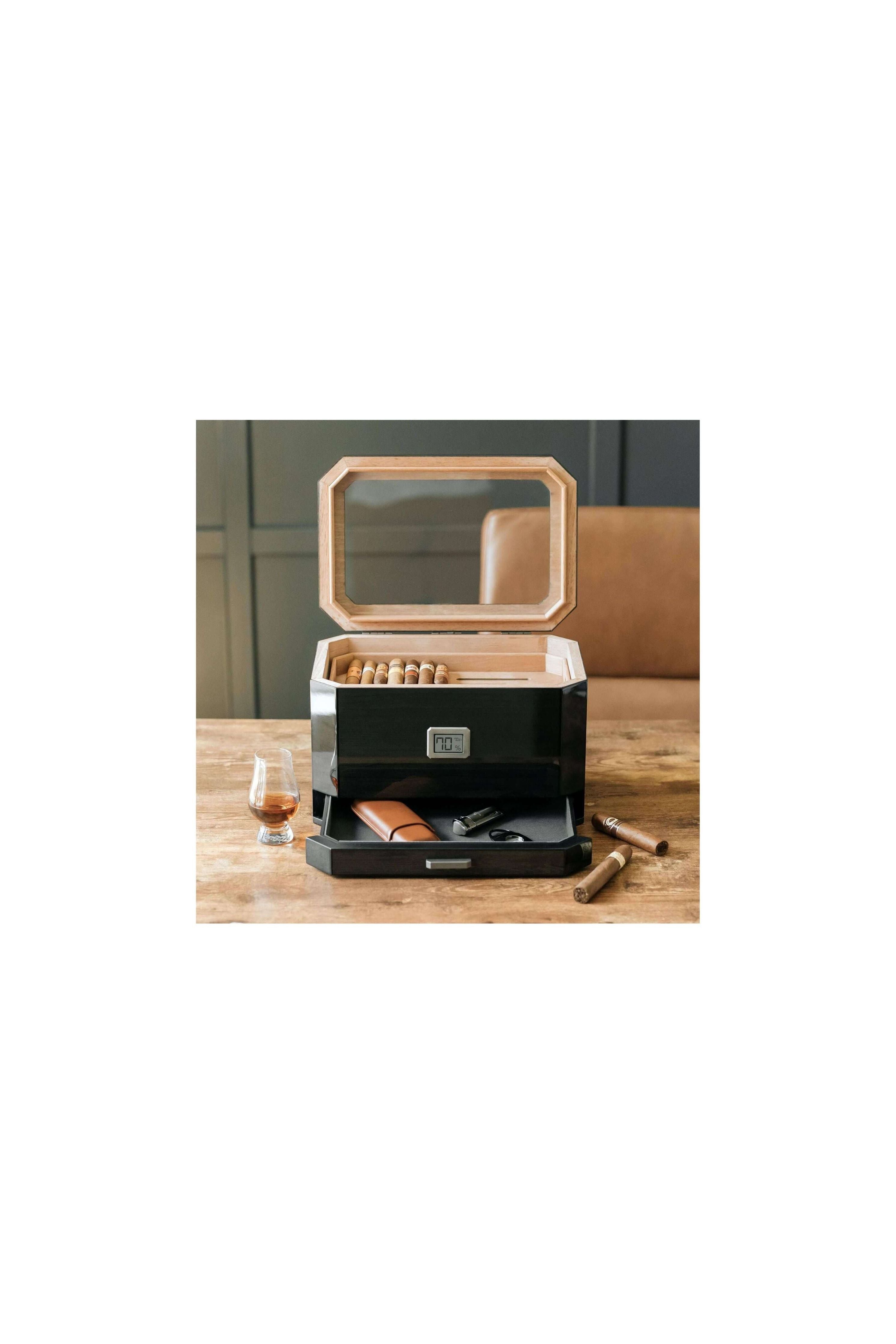 Humidor à couvercle en verre Octodor avec cigares, verre à whisky et accessoires sur une table en bois.