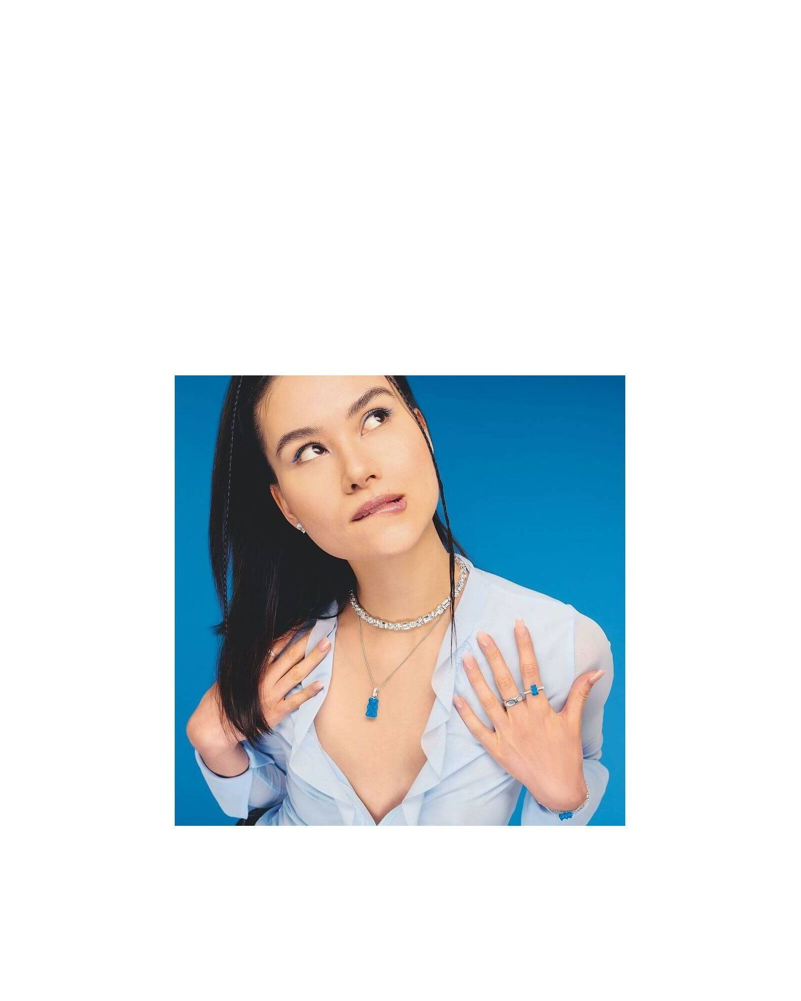 Modèle portant une chaîne à breloque Ours en argent et cristal bleu, avec accessoires assortis sur fond bleu.