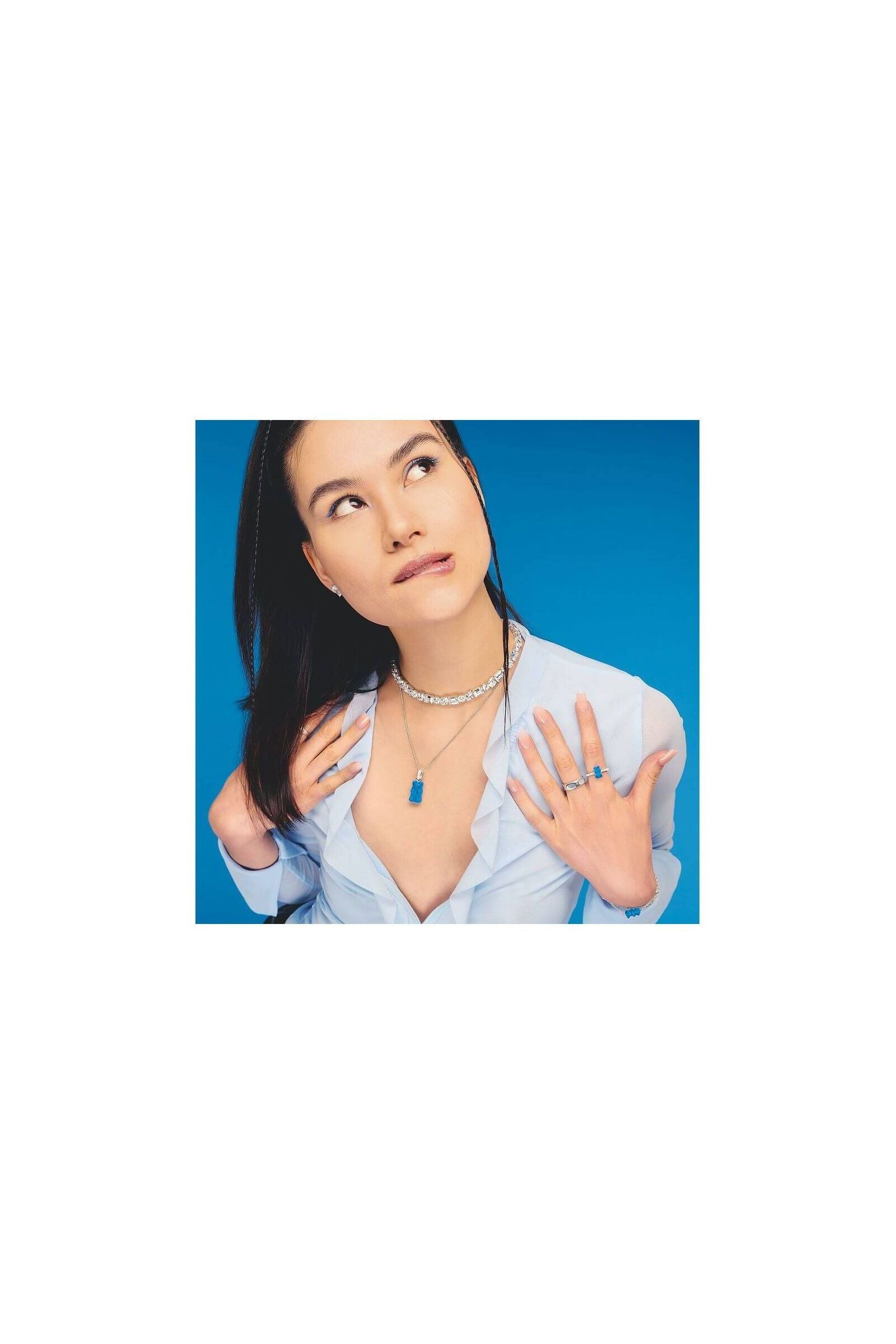 Modèle portant une chaîne à breloque Ours en argent et cristal bleu, avec accessoires assortis sur fond bleu.