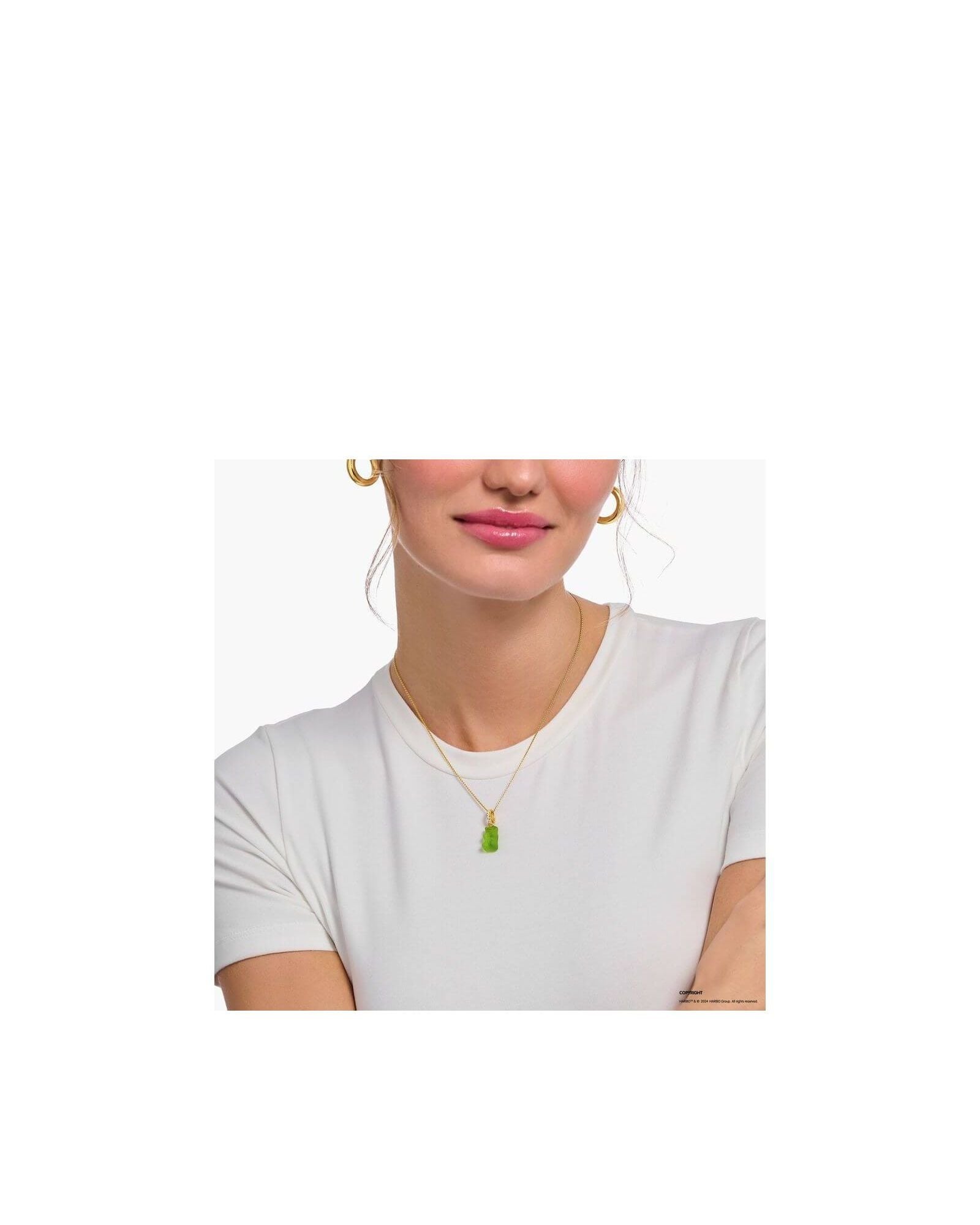 Gold chain necklace with green bear charm worn by a woman in a white shirt.
