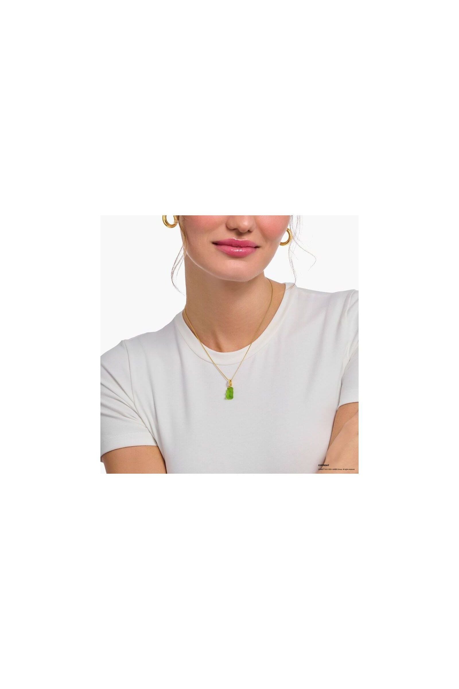 Gold chain necklace with green bear charm worn by a woman in a white shirt.