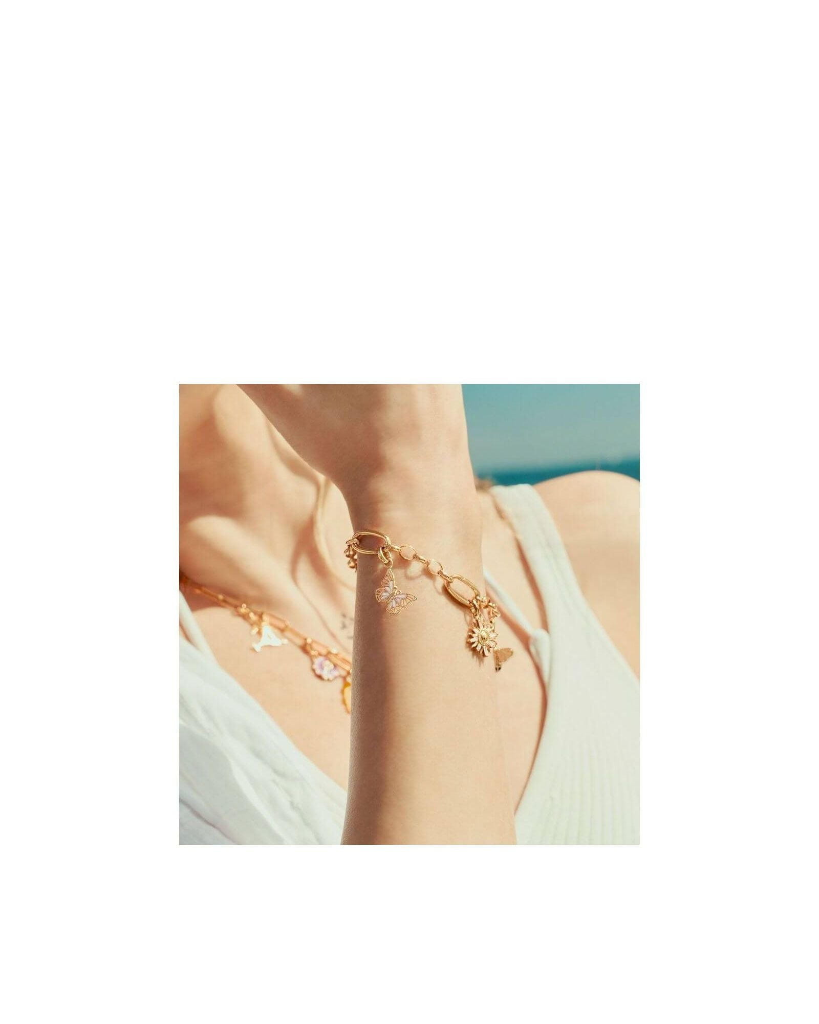 Pendentif charm papillon en plaqué or, porté sur bracelet délicat, capturant l'élégance estivale.