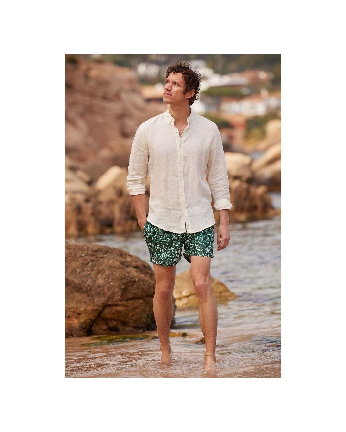 Homme en chemise en lin nature, marchant sur la plage avec un pantalon court, ambiance décontractée.