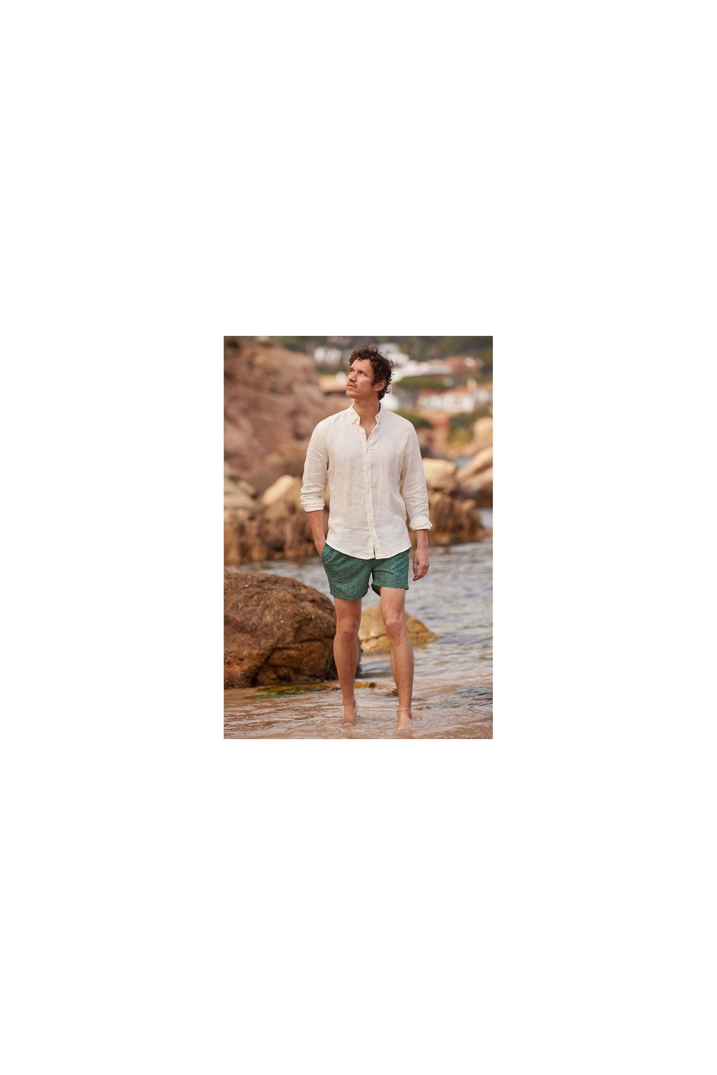 Homme en chemise en lin nature, marchant sur la plage avec un pantalon court, ambiance décontractée.