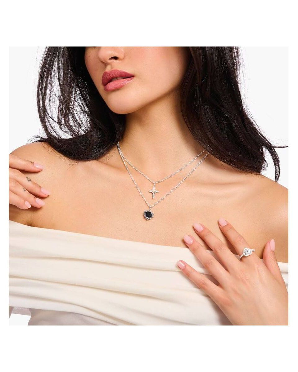 Femme portant une chaîne avec pendentif cœur noir et croix en argent sur un décolleté élégant.