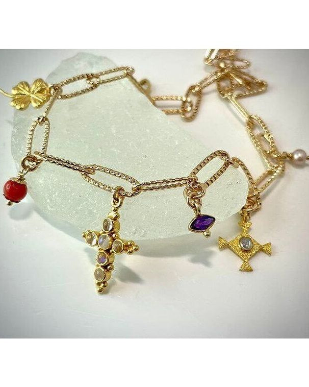 Collier Mystique en plaqué or 24 carats, orné de pendentifs croix et pierres colorées, sur fond de pierre blanche.