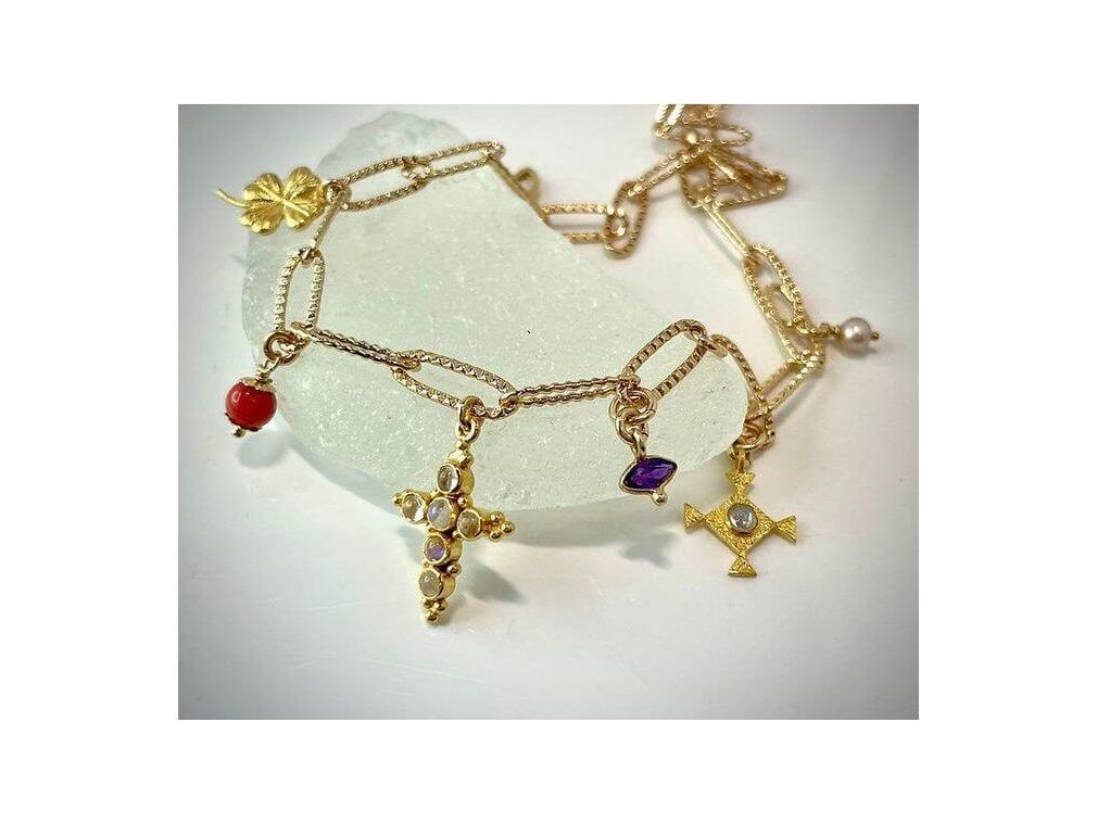 Collier Mystique en plaqué or 24 carats, orné de pendentifs croix et pierres colorées, sur fond de pierre blanche.