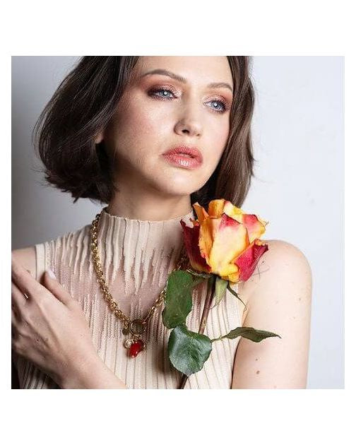 Model showcasing Collier Madone necklace with coral bead, styled with a vibrant rose.