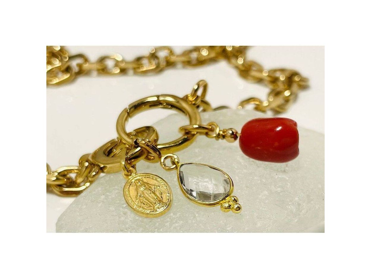 Collier Madone bracelet featuring gold links, red coral bead, and a clear gem on a light stone background.