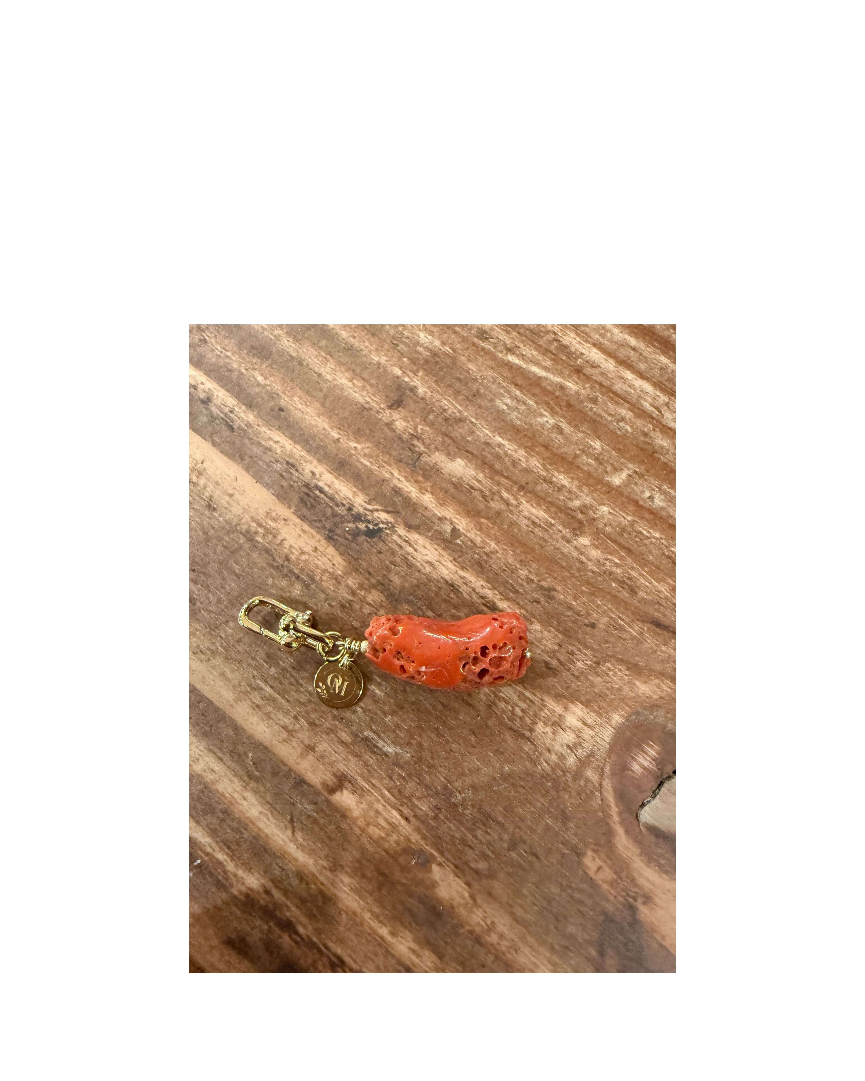 Pendentif corail brut naturel de la mer Méditerranée avec attache dorée sur fond en bois.