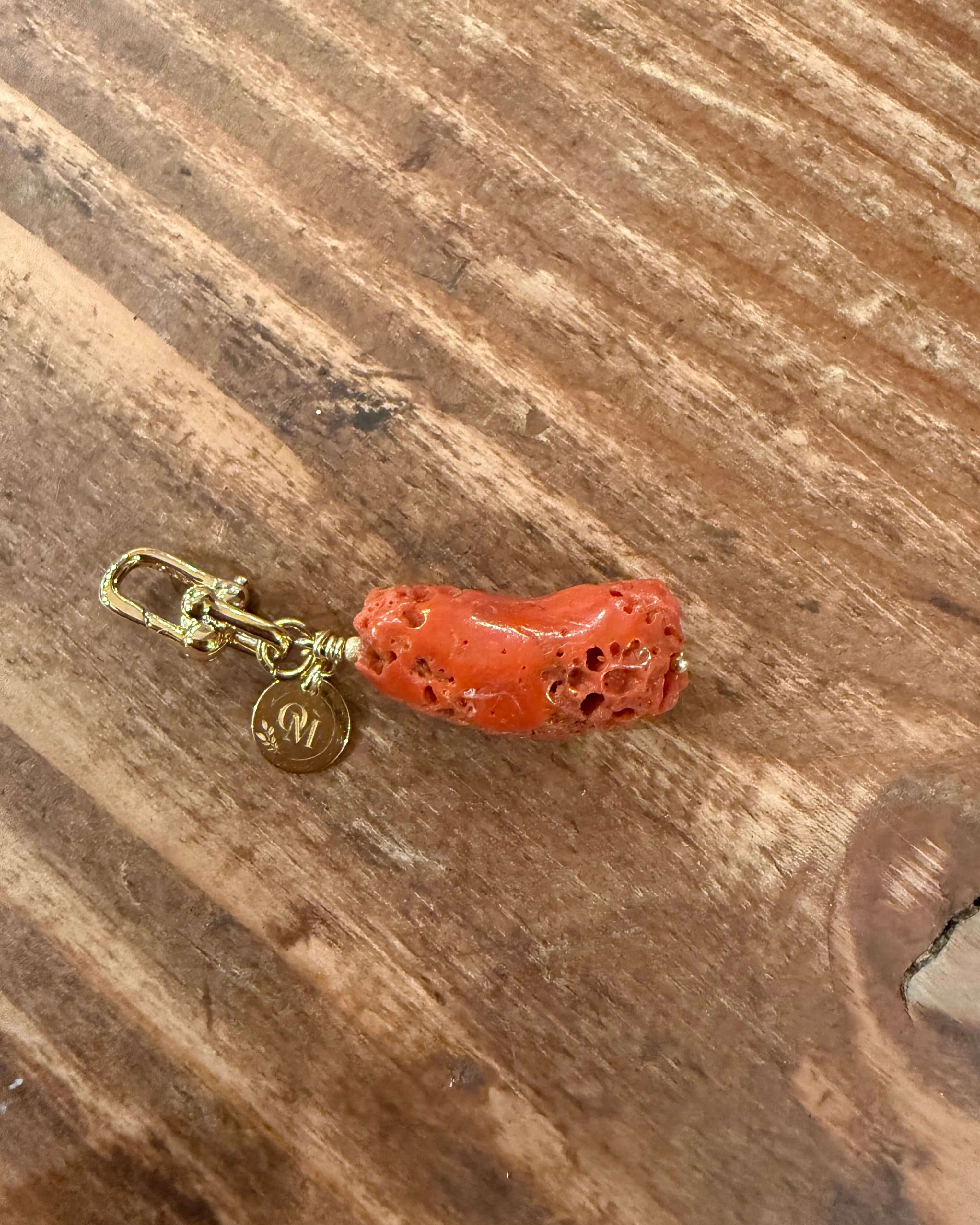 Pendentif corail brut naturel de la mer Méditerranée avec attache dorée sur fond en bois.