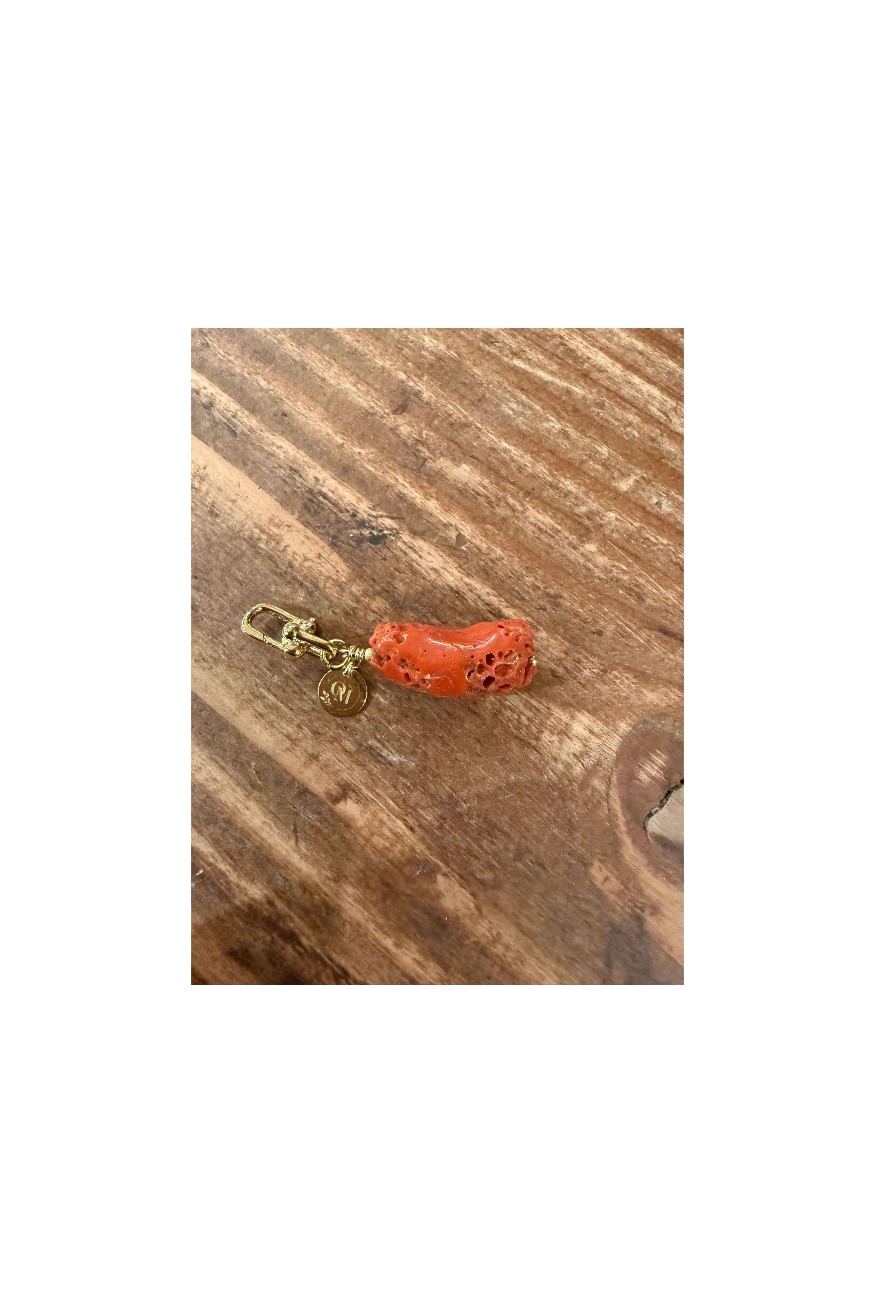 Pendentif corail brut naturel de la mer Méditerranée avec attache dorée sur fond en bois.