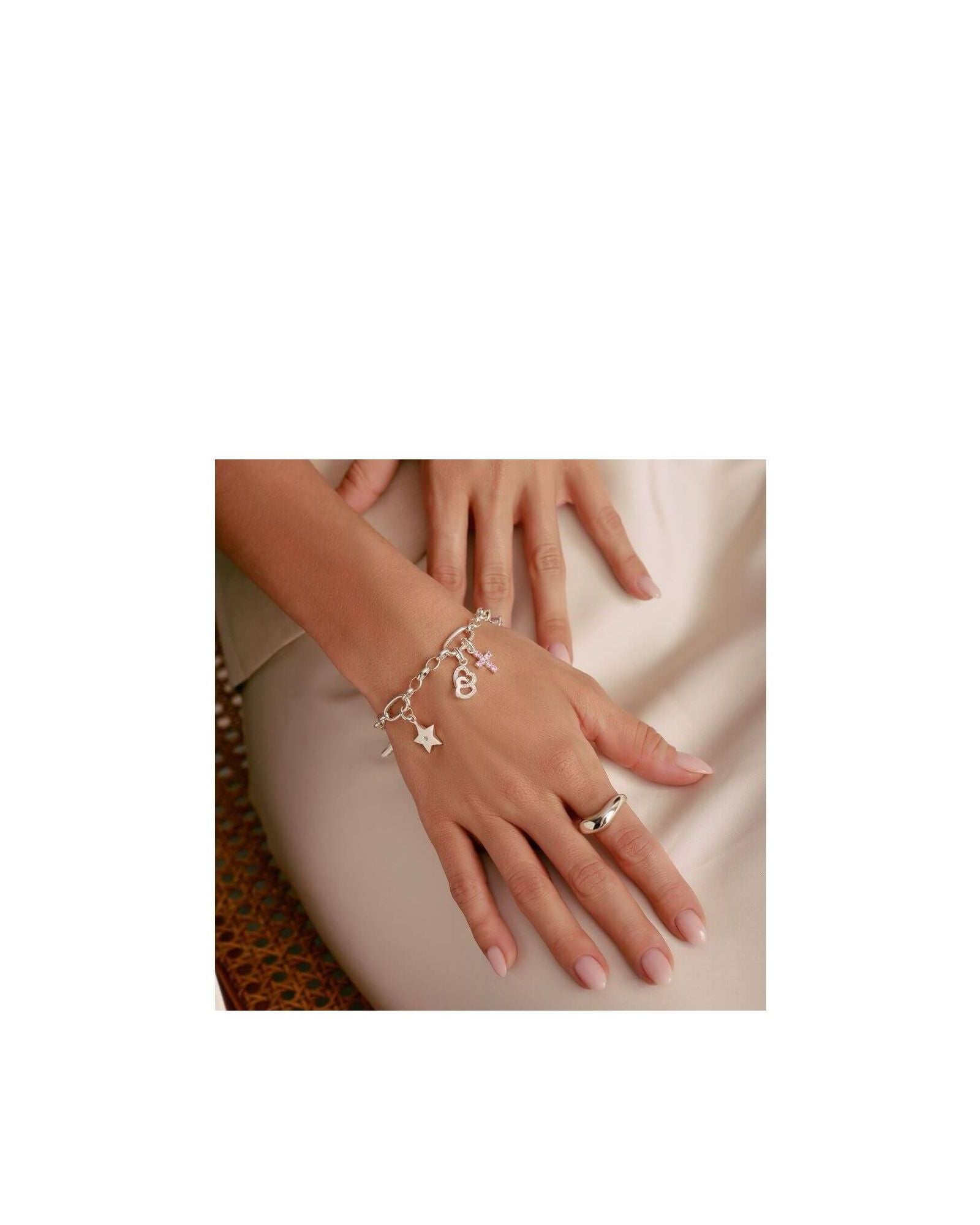 Bracelet charm argent avec étoile, croix et cœur, porté sur une main élégante, mettant en valeur un style unique.