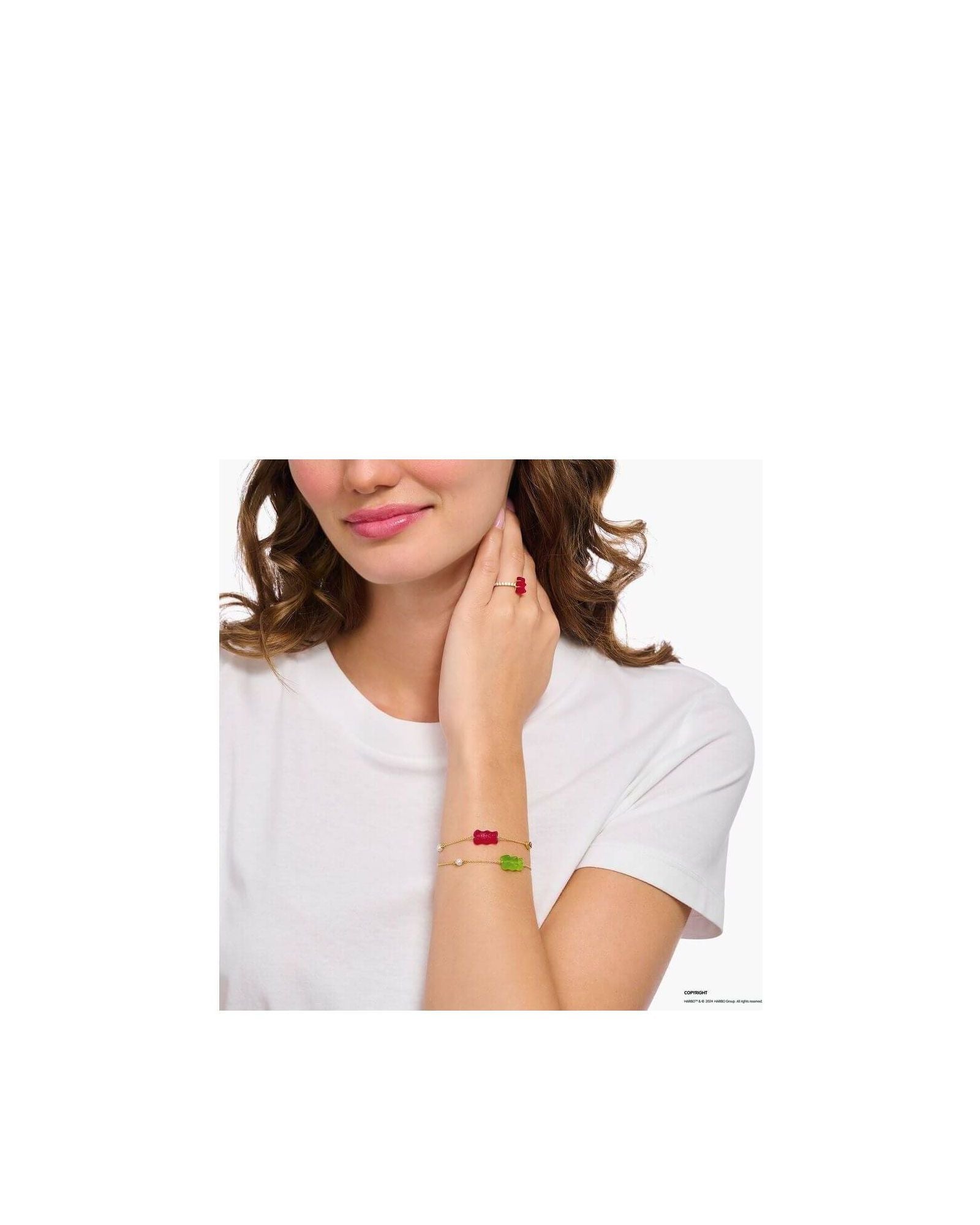Woman wearing bracelets with colorful bear charms, one red and one green, against a plain white t-shirt.
