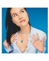 Model showcasing elegant jewelry against a blue background, featuring layered necklaces and rings.