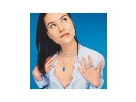 Model showcasing elegant jewelry against a blue background, featuring layered necklaces and rings.