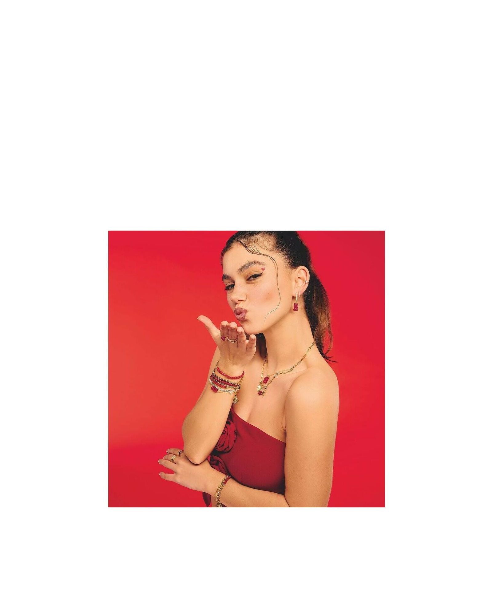 Femme faisant un geste de baiser, portant un bracelet avec Ours d’or rouge et autres bijoux raffinés.