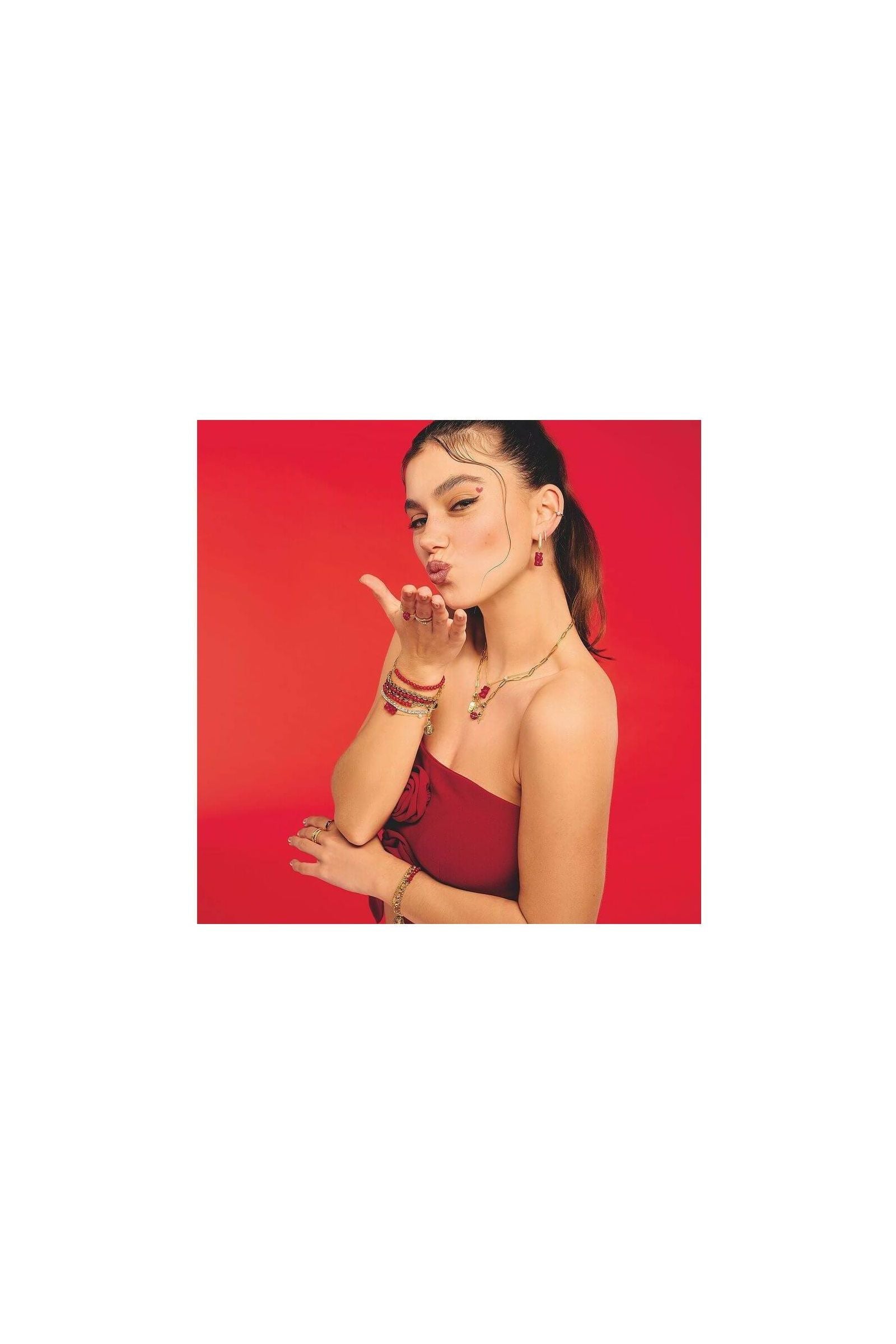 Femme faisant un geste de baiser, portant un bracelet avec Ours d’or rouge et autres bijoux raffinés.