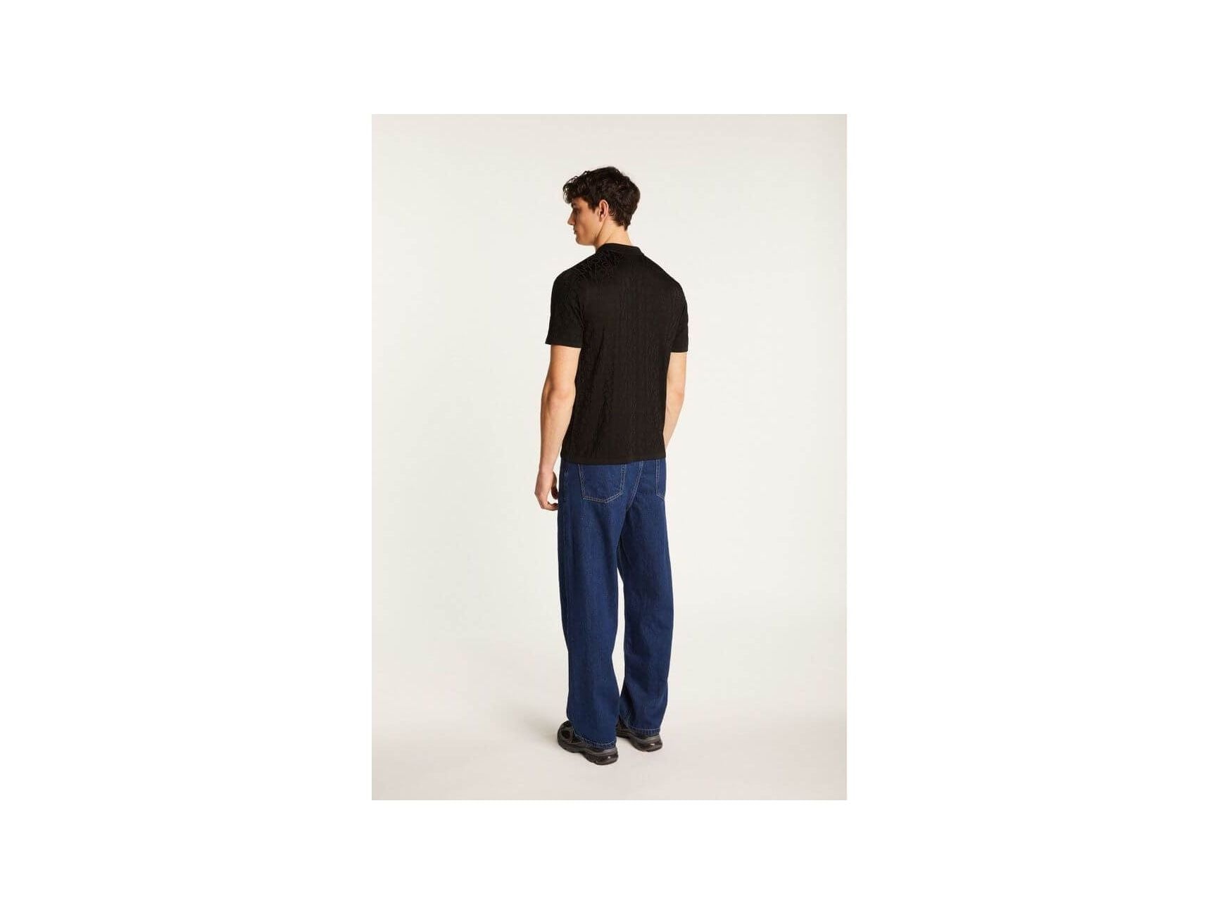 Homme de dos portant une chemise noire avec un pantalon bleu, montrant un style moderne et décontracté.