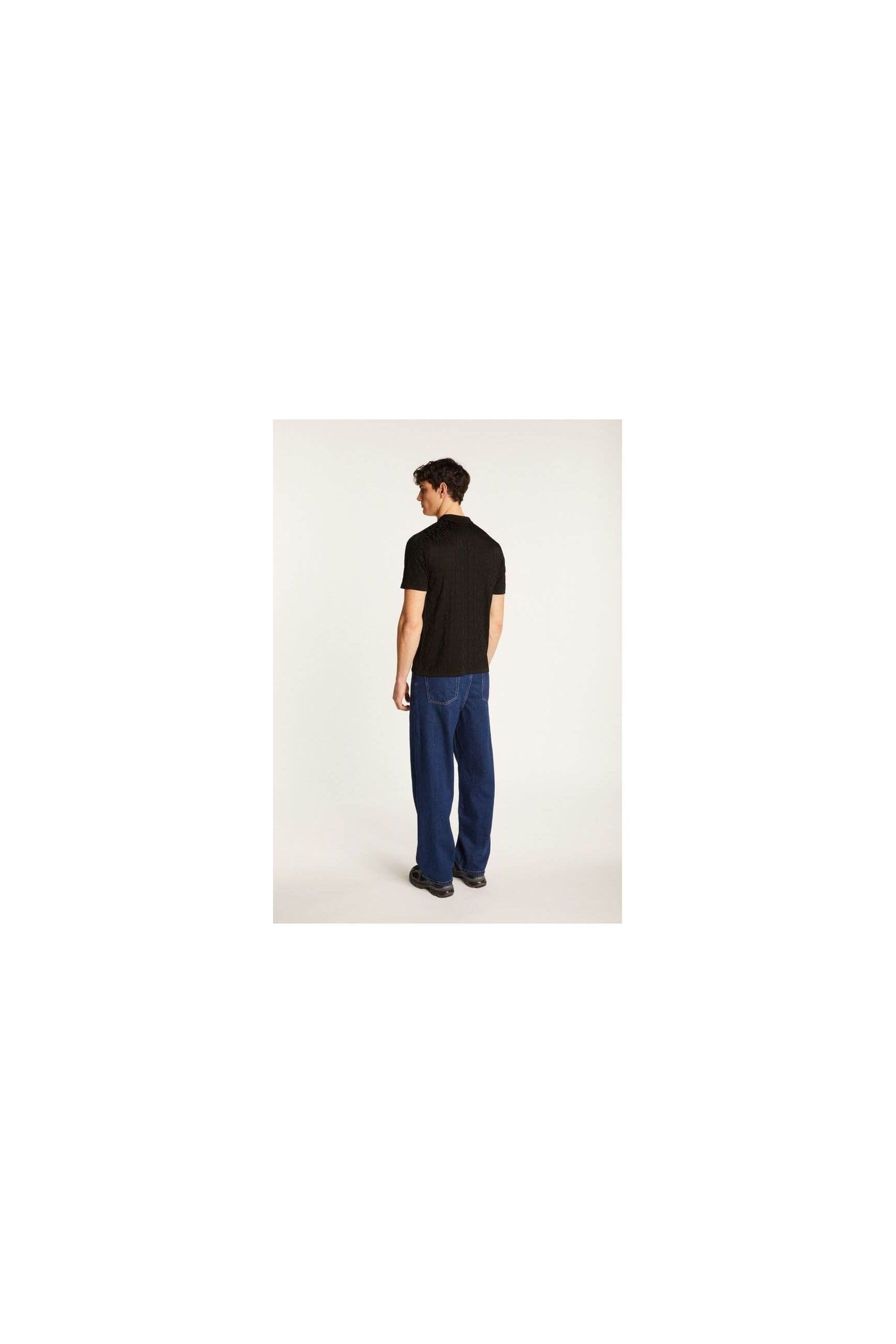 Homme de dos portant une chemise noire avec un pantalon bleu, montrant un style moderne et décontracté.