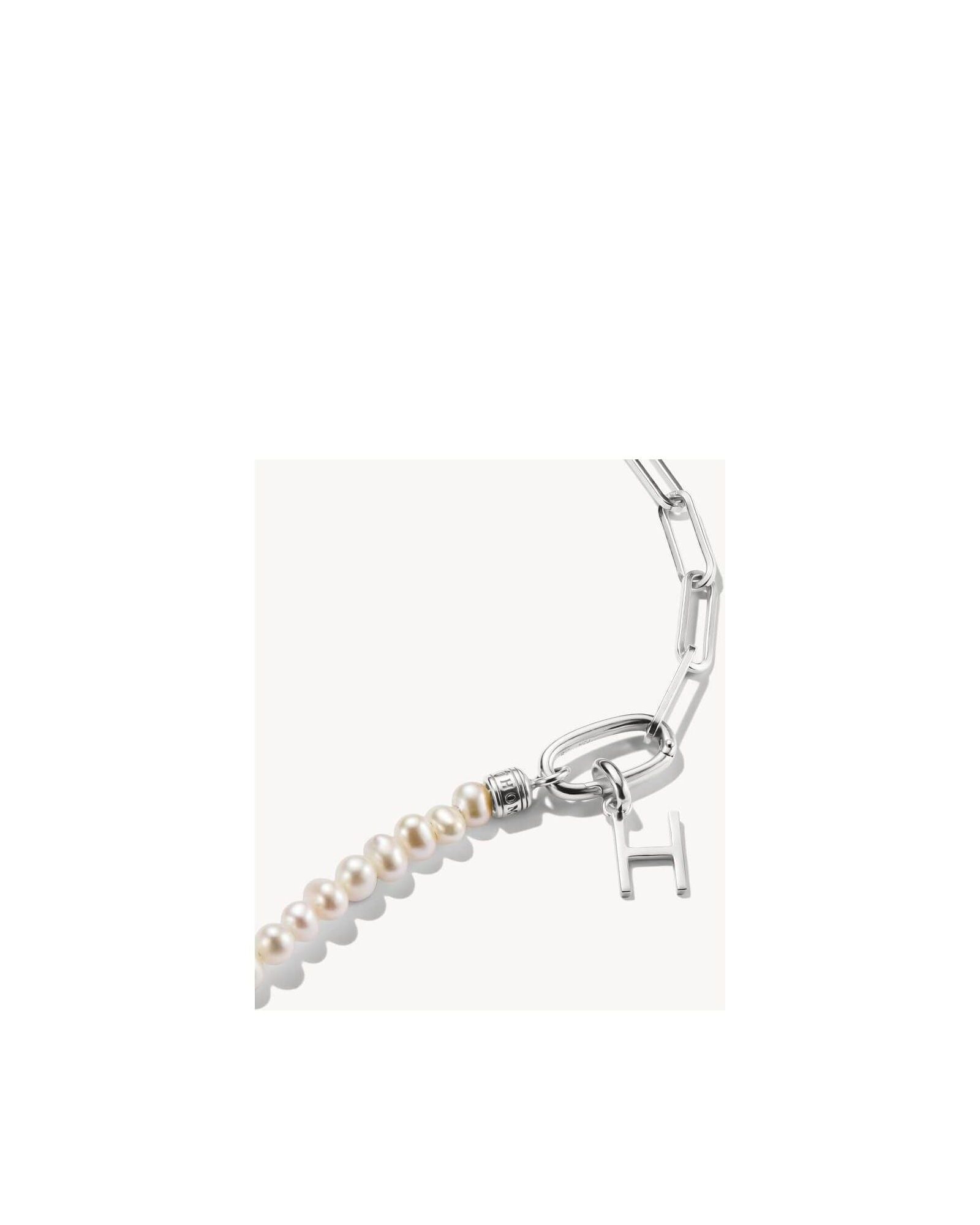 Close-up of a silver charm pendant with a letter 'H' and pearls, perfect for personalized jewelry.