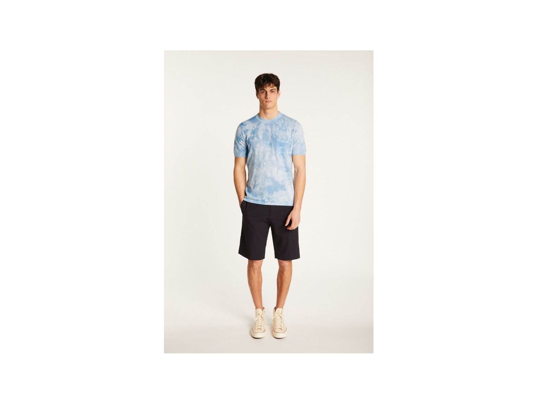 Model wearing a light blue tie-dye T-shirt paired with dark shorts and sneakers.