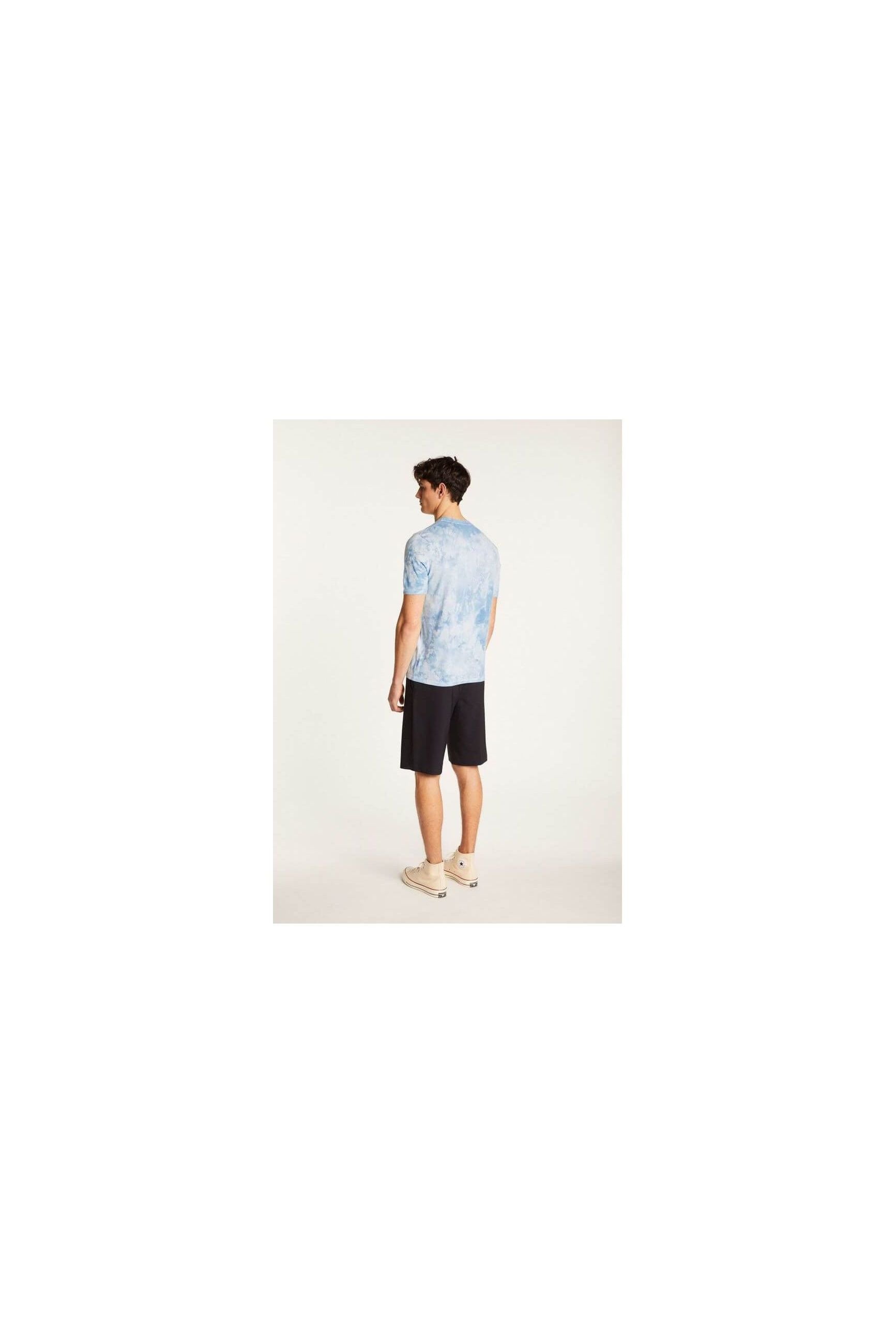 Man wearing a light blue tie-dye T-shirt and black shorts, showcasing a modern casual style from the back.