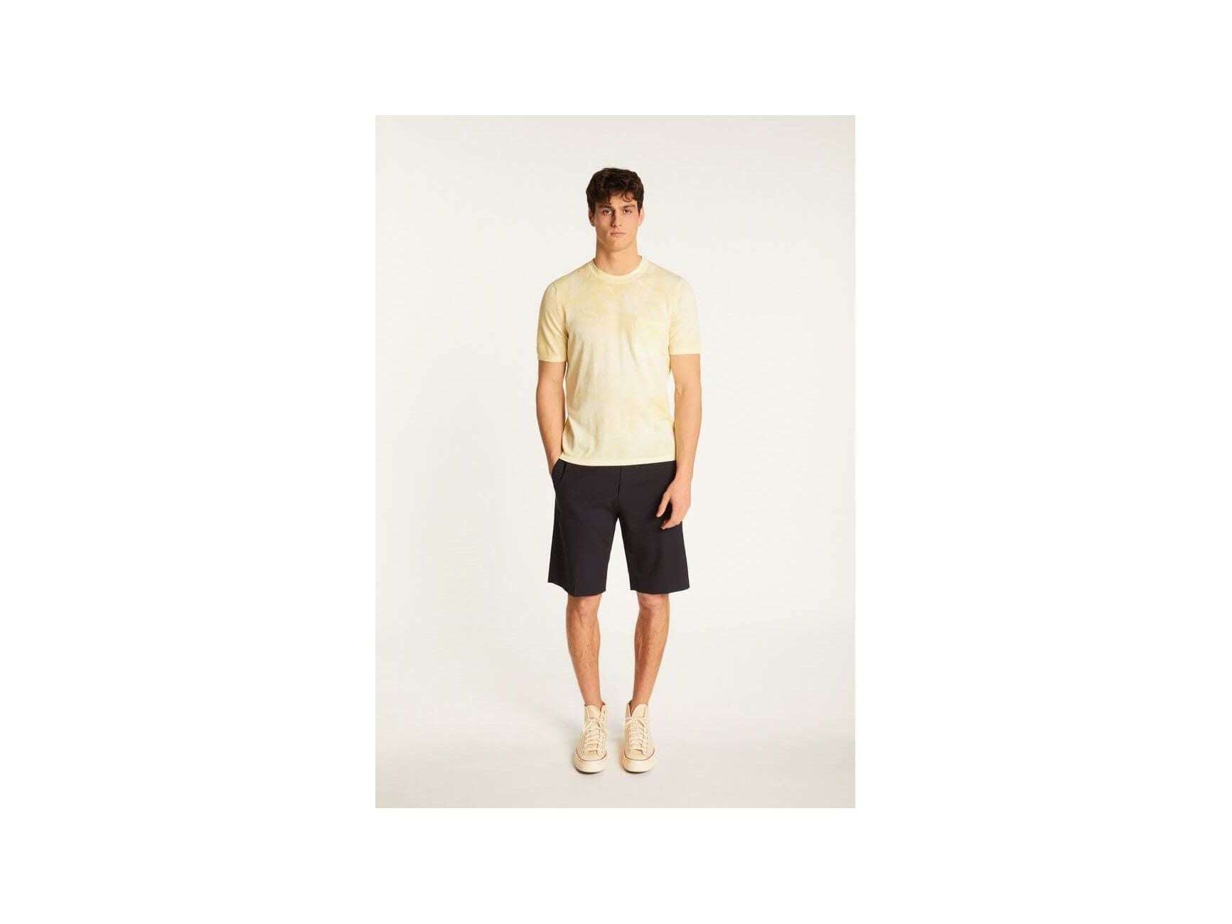 Homme portant un t-shirt jaune clair et un short noir, mettant en avant un look décontracté et élégant.
