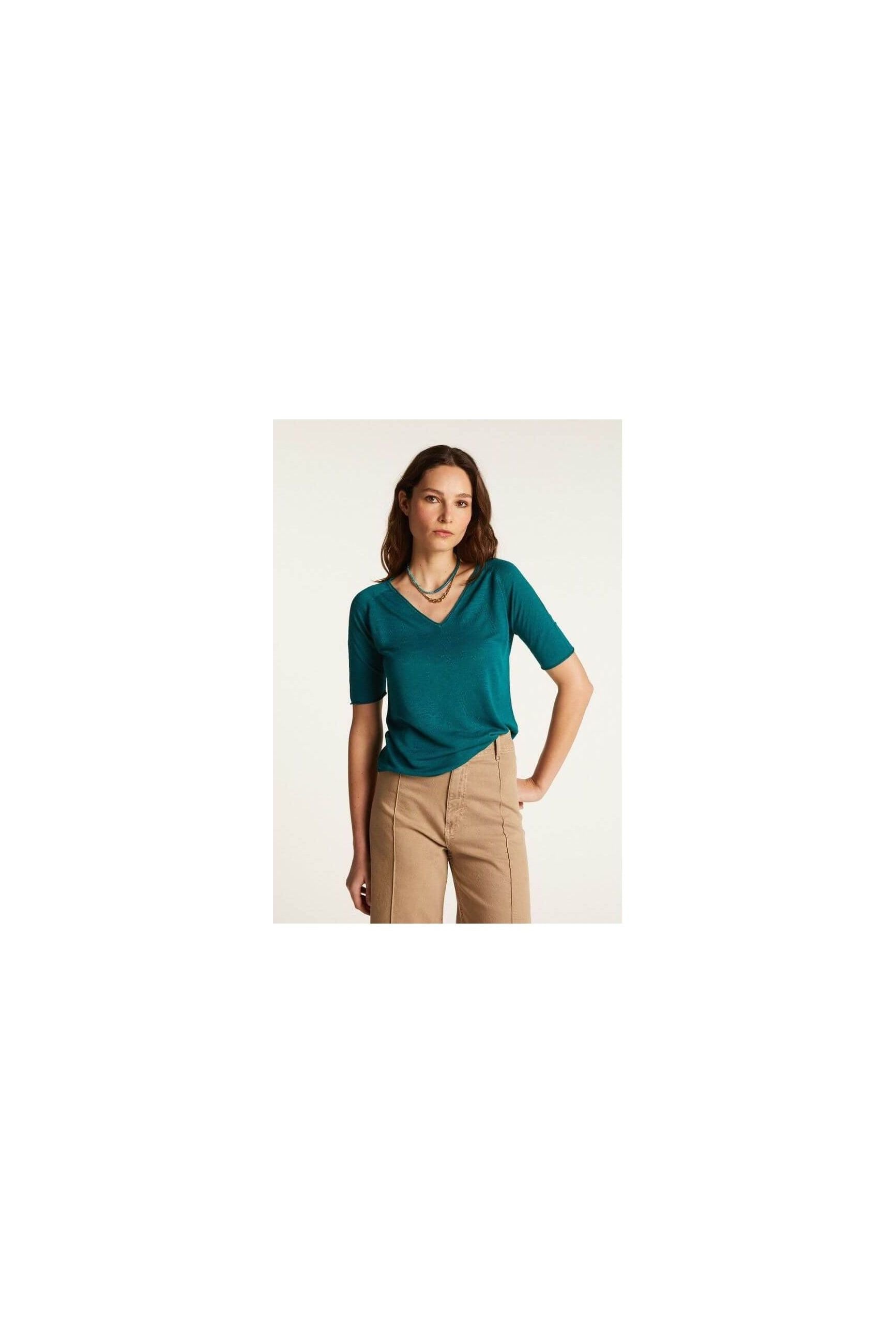 Femme portant un T-shirt teal à col V, en lin léger, associé à un pantalon beige.