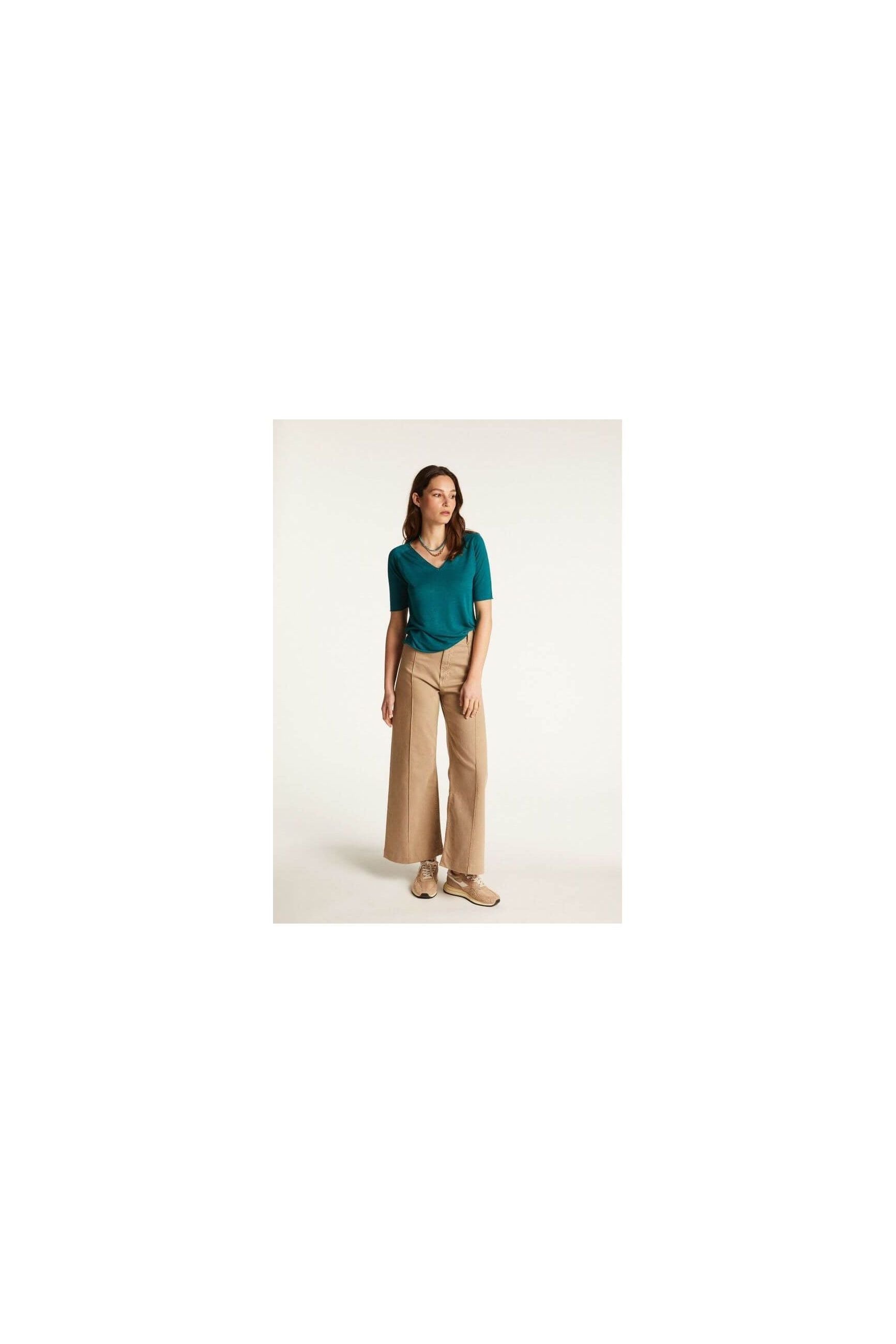 Modèle féminin en t-shirt turquoise et pantalon large beige, parfaite tenue décontractée pour l'été.