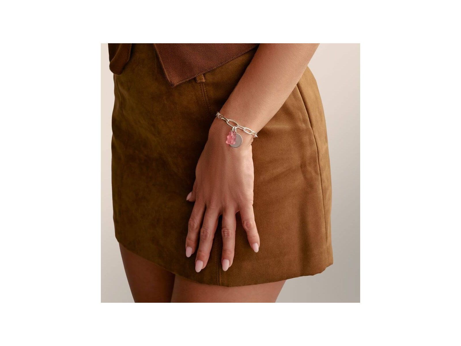 Femme portant un bracelet charm en argent recyclé avec des breloques colorées, sur une jupe marron.