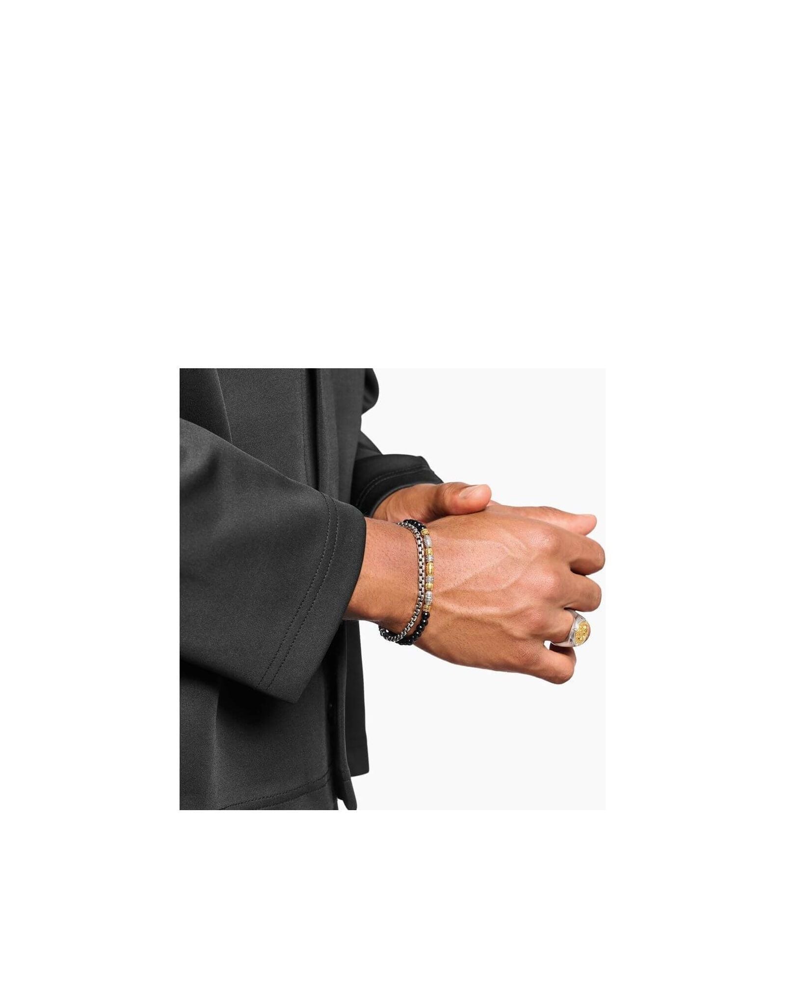 Homme portant un bracelet en argent et des accessoires de mode élégants sur une chemise noire.