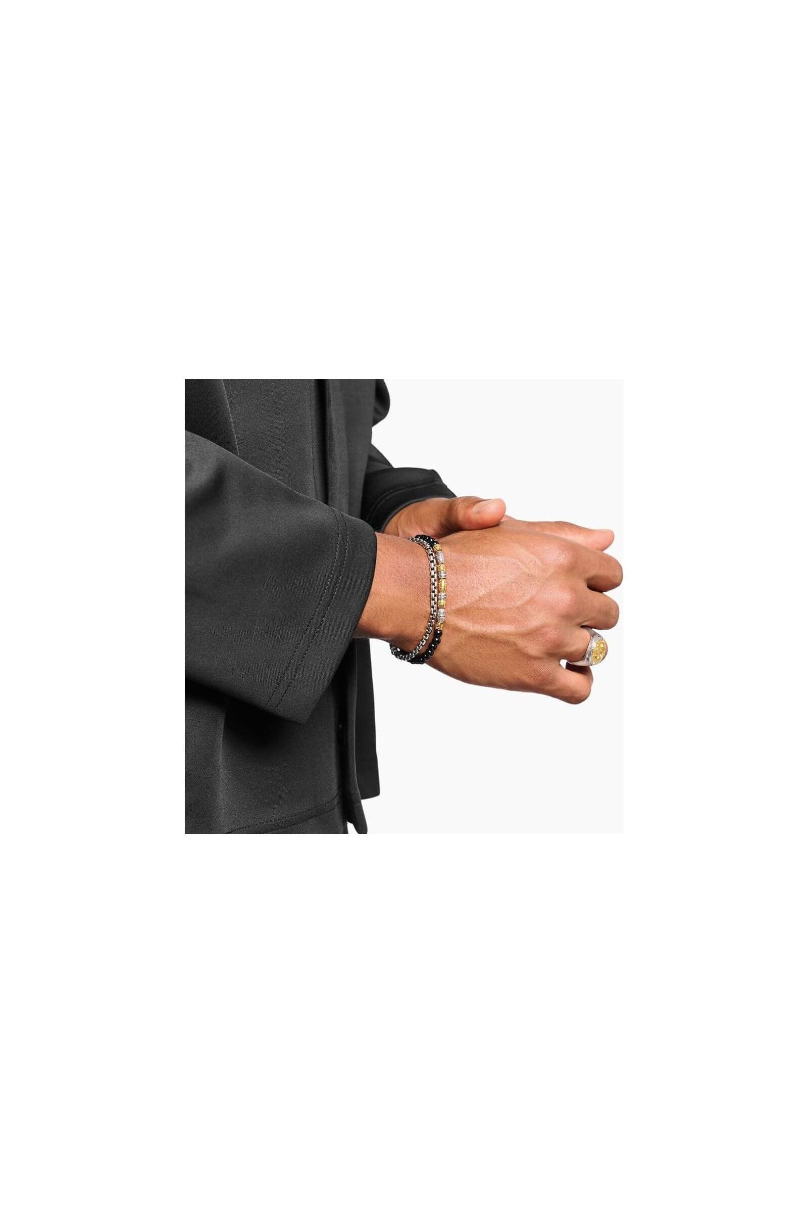 Homme portant un bracelet en argent et des accessoires de mode élégants sur une chemise noire.